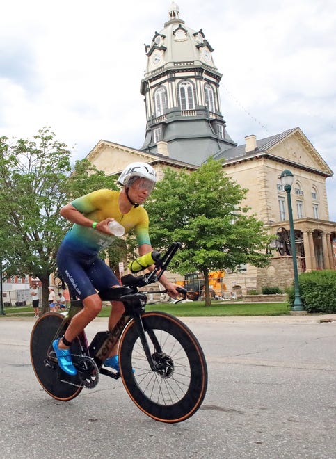 A competitor picks up water as he races by the Madison County Courthouse on John Wayne Drive in Winterset during the Ironman North American Championship 140.6-mile Des Moines Triathlon as athletes compete in a 2.4-mile swim at Gray’s Lake, 112-mile bike race, and a 26.2-mile run in Des Moines on Sunday, June 12, 2022. This regional competition will offer qualifying slots to the 2022 Ironman World Championship in Kailua-Kona, Hawaii in early October 2022.