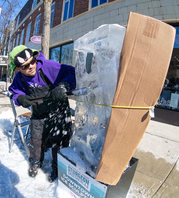 Ice carver Ted Bonde, of Kiel, Wis., chisels out what he says will be a bluegill in ice during the Sturgeon Spectacular, Saturday, February 11, 2023, in Fond du Lac, Wis. He used a piece of cardboard to prevent the sun from harming his carving ice block.
